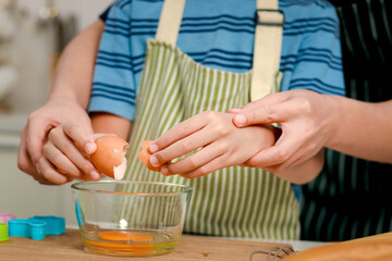 Closeup of father and son kid hands cracking an egg into glass bowl, dad and boy with apron cooking meal together at kitchen, parent helping child with cracking egg, lovely family chef cooking food.