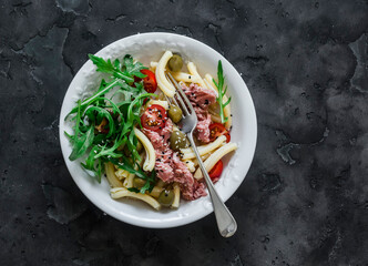 Pasta with canned tuna, olives and cherry tomatoes on a dark background, top view