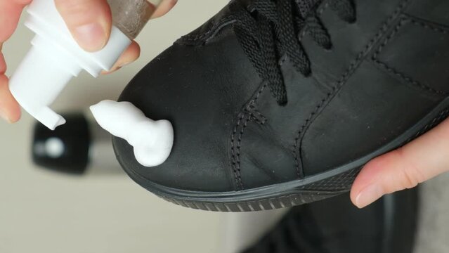 Applying cleaning foam from a bottle to nubuck men's shoes