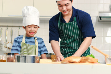 Happy smiling Asian father and son kid with apron and chef hat cooking meal together at kitchen, dad parent and boy child cutting bread into various shapes with cutters, cute family chef cooking food.