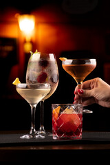 cocktail collection with vesper negroni weesky and lillet with berries and mint in bar rubber holder with blurred pub background and female hand picking one of them