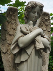 An angel with a dove. Sculpture in the cemetery. The figure of an angel with wings holding a bird in his arms. Lamentation for the deceased. Headstone monument on a Christian grave. Sadness and