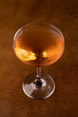 Cocktail glass with whiskey and orange peel garnish seen from above on wooden table