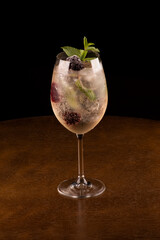 glass of refreshing cocktail with mint and berries and ice isolated on wooden table with dark background close-up