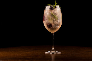 glass of refreshing cocktail with mint and berries and ice isolated on wooden table with dark background from the front