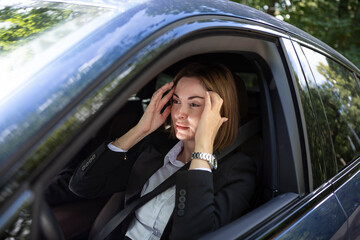 Young attractive businesswoman in suit driving and standing in a traffic jam. Tired business lady sitting in car and feeling bad because of long time of traffic light