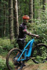Naklejka premium Mountain bike cyclist in sport equipment and helmet riding on rugged trails