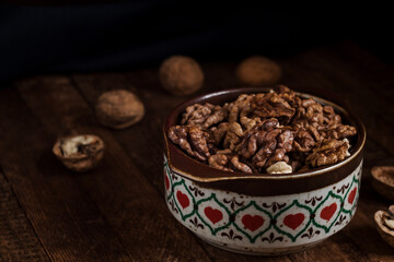 Organic dried walnut kernels in a ceramic bowl on a wooden background.