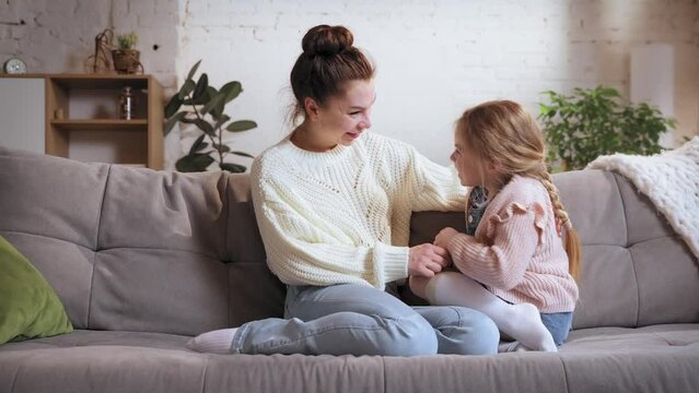 Trusting talks. Beautiful woman, young mother and little girl, kid sitting on couch at home on daytime and talking. Concept of family relationship, motherhood and childhood, love, caring