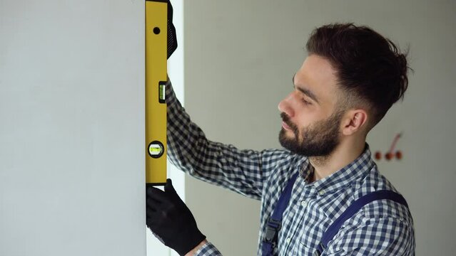 Young engineer builder measures of the vertical deviation of the wall. Bubble level ruler close up view, measuring and leveling concept