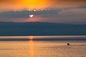 Nad Morzem Martwym w Jordanii o zachodzie słońca. Piękny zachód słońca lekko przysłonięty chmurą, ponad wzgórzami nad spokojnym Morzem Martwym. - obrazy, fototapety, plakaty
