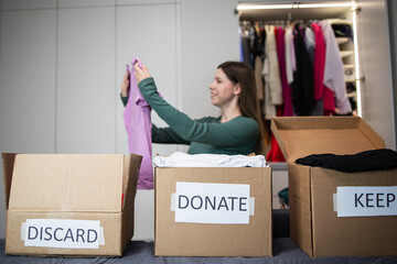 Unrecognizable woman sorts through her wardrobe. Three craft cardboard boxes of keep, discard,...