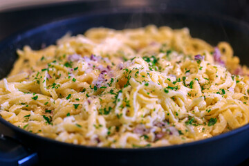 schwäbische Kässpätzle mit Zwiebeln und Kräutern dünsten in einer Pfanne