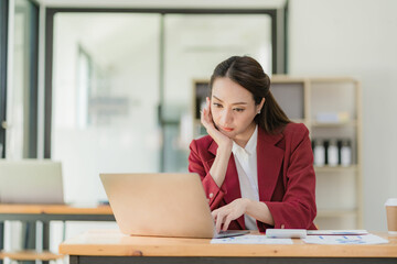 Smiling Asian businesswoman working on tablet computer at her desk in bright modern office Calculating financial report expenses with graph documents