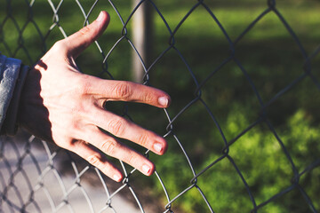 A person's hand is touching a chain link fence.