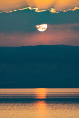 Nad Morzem Martwym w Jordanii o zachodzie słońca.  Pionowe ujęcie pięknego zachodu słońca ponad wzgórzami nad spokojnym Morzem Martwym. - obrazy, fototapety, plakaty