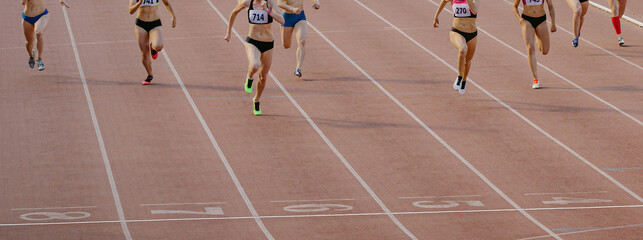 group female athletes run sprint race on stadium track, woman runner winner distance is approaching finish line