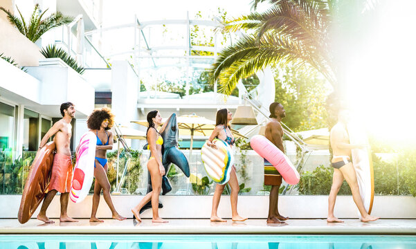 Trendy friends walking at swimming pool party with lilo airbed and swim wear - Vacation life style concept with happy guys and girls having fun on summer day at luxury resort - Bright vivid filter