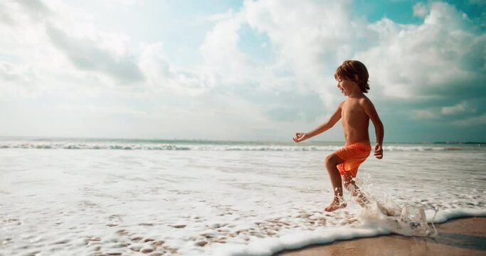 Boy running on the waves in summer warm day with smile and laugh