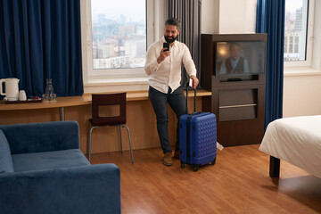 Contented tourist with mobile phone and baggage in hotel room