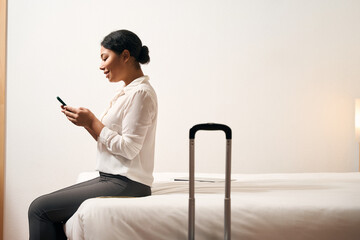 Pleased businesswoman using her mobile phone in hotel room