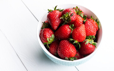 Bowl of fresh strawberries on a white wooden table. Fresh ripe delicious strawberries in a white bowl on a wooden background. 