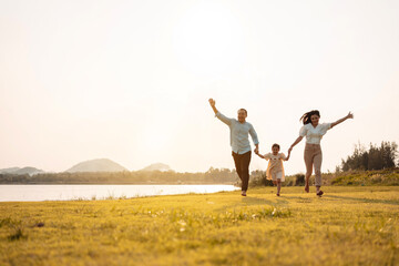 Happy Family enjoying a peaceful walk and running in a scenic field with a serene lake in the background.