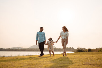 Happy Family enjoying a peaceful walk and running in a scenic field with a serene lake in the background.