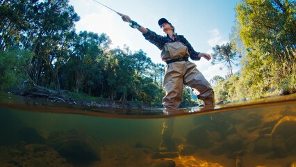 Woman angler on the river. Woman stands in the water in waders and casts the line. Woman fishing on the river - 589948002
