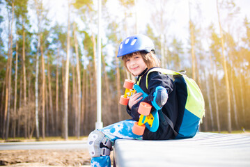 happy child schoolboy in a protective helmet and with a backpack sits and hugs a bright plastic...