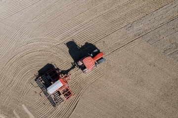A grain seeder attached to a tractor sows grain in the field. Top view of modern equipment. Sowing grain.