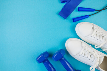 The concept of fitness, sport. Top view photo of white sports shoes, elastic bands and blue dumbbells