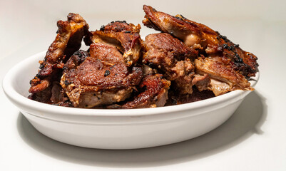 Heap of grilled lamb chops on oval white bowl, with white background.