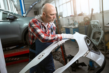 Employee of a car workshop examines part of car body