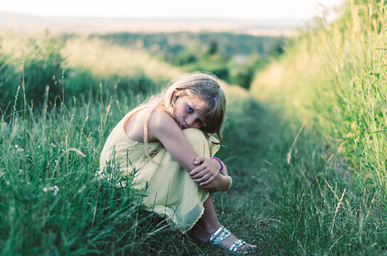 sad child outdoors in countryside sitting in grass