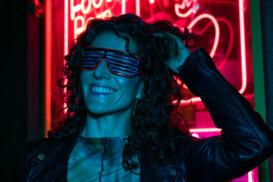 Fashionable woman dancing in room with colorful lamps. Cyberpunk style or hipster with fluorescent glasses. Night club, futuristic outfit. Sexy lady concept