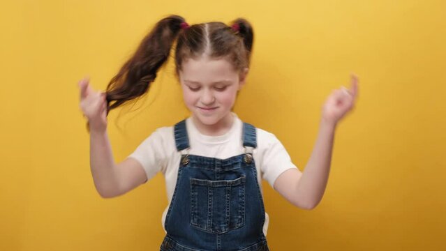 Portrait of overjoyed little girl kid showing rock n roll gesture by hands, shouting yeah with crazy expression, dancing, rejoicing in success, isolated on yellow studio background. Cool sign concept