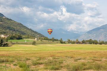 hot air balloon suspended over a green landscape next to Quart, Aosta Valley, Italy