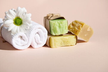 Spa set with two rolled white towels, chamomile flower and stack of organic natural soap bars with natural ingredients on isolated beige background. Horizontal shot. Still life. Copy advertising space