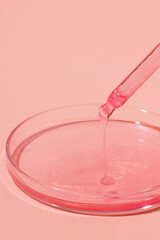 Pipette with dripping pink liquid. Or rose gold. On top of a Petri dish with pink liquid. On a pink background. Laboratory, chemistry, medicine. Cosmetic research. glitter.