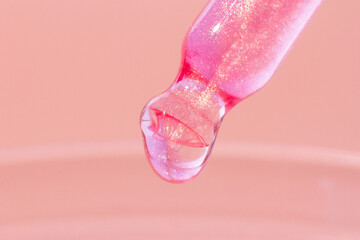 Pipette with dripping pink liquid. Or liquid rose gold. Close-up. On a pink background. Laboratory, chemistry, medicine. Cosmetic research. shine.