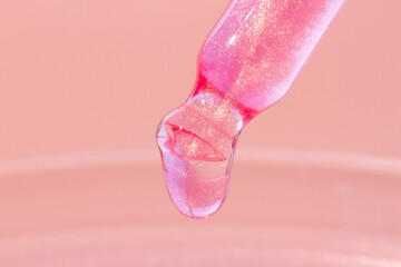 Pipette with dripping pink liquid. Or liquid rose gold. Close-up. On a pink background. Laboratory, chemistry, medicine. Cosmetic research. shine.