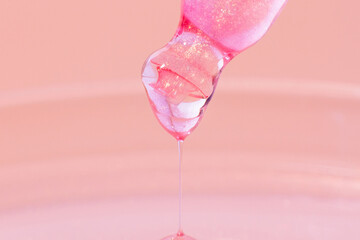 Pipette with dripping pink liquid. Or liquid rose gold. Close-up. On a pink background. Laboratory, chemistry, medicine. Cosmetic research. shine.