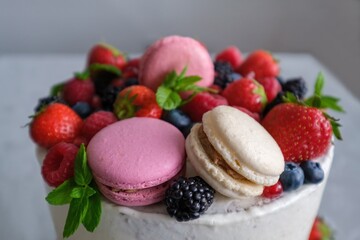 Birthday or anniversary cake with cream cheese frosting decorated with macaroons, fresh raspberries, strawberries, blackberries and blueberries. 