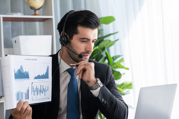Business man wearing headphone present financial data or BI paper via laptop during online meeting....