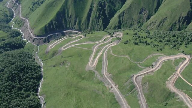 Aerial top down drone shot above the winding mountain road between the trees near Khevsureti's Aragvi, Georgia
