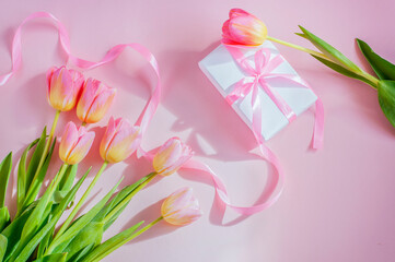 Obraz na płótnie Canvas gift tied with a long pink ribbon and tulips on a pink light background. High quality photo