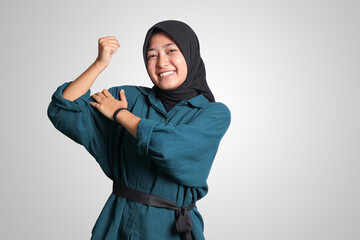 Portrait of excited Asian muslim woman with hijab showing strong biceps, demonstrating strength. Isolated image on white background