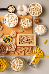 Nutritional supplements, organic minerals and many different vitamins such as vitamin a, d3, c, e, b in small glass jars and plates on wooden desk from above on light background in rustic style. 