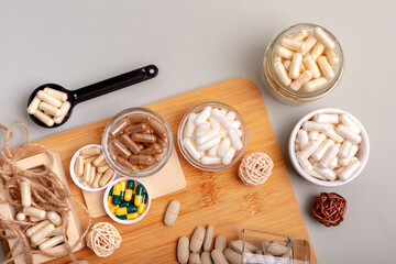 Nutritional supplements, organic minerals and many different vitamins such as vitamin a, d3, c, e, b in small glass jars and plates on wooden desk from above on light background in rustic style. 